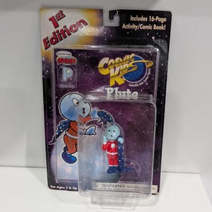 Könnte beinhalten: Cosmic Kids Pluto Actionfigur in einer transparenten Kunststoffverpackung. Die Figur trägt einen rot-weißen Raumanzug mit blauem Umhang. Die Verpackung enthält den Text "1st Edition" und "Includes 16-Page Activity/Comic Book!"