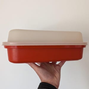 Op de afbeelding: Een rechthoekige opbergbak met een dieporanje onderkant en een doorschijnend, gebroken wit deksel. De bak heeft een brede rand aan de bovenkant waar het deksel stevig op rust. Het ontwerp is eenvoudig, functioneel en heeft afgeronde hoeken.