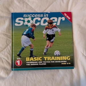 May include: A book titled "Success in Soccer" with a cover featuring two young soccer players on a green field. The cover also includes the text "Basic Training" and "Ages 6-14".