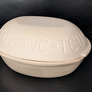 Può includere: Pentola per microonde in ceramica bianco sporco con coperchio a cupola. Il coperchio presenta la scritta in rilievo "Wave-teur". La pentola è progettata per l'uso nel microonde e ha una forma arrotondata.