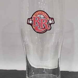 May include: A white ceramic mug with a black handle and the text "But First, Coffee" in a black, handwritten-style font. The mug is on a white surface.