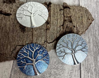 May include: Three round metal tree of life ornaments. One is silver, one is light blue, and one is a gradient of light blue to white.