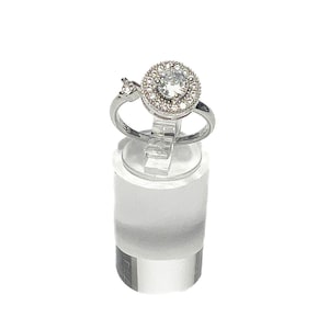 May include: A silver ring with a large round clear stone surrounded by smaller clear stones. The ring has a smaller clear stone on the side.