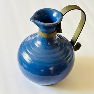 May include: A blue ceramic pitcher with a metal handle. The pitcher has a rounded body and a wide mouth.