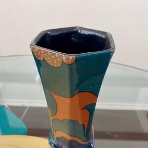 K&ouml;nnte beinhalten: Eine blaue und orangefarbene Keramikvase mit geometrischem Design. Die Vase hat eine sechseckige Form und eine breite &Ouml;ffnung.