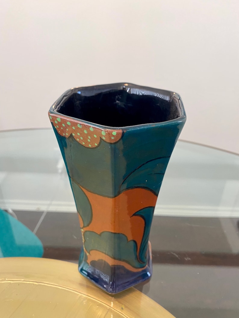 K&ouml;nnte beinhalten: Eine blaue und orangefarbene Keramikvase mit geometrischem Design. Die Vase hat eine sechseckige Form und eine breite &Ouml;ffnung.