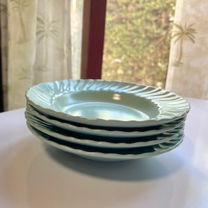 May include: A stack of four light blue ceramic salad plates with a scalloped edge.