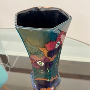 K&ouml;nnte beinhalten: Eine dunkelblaue und gr&uuml;ne Keramikvase mit geometrischer Form und floralem Design. Die Vase ist mit roten, violetten und wei&szlig;en Blumen verziert.