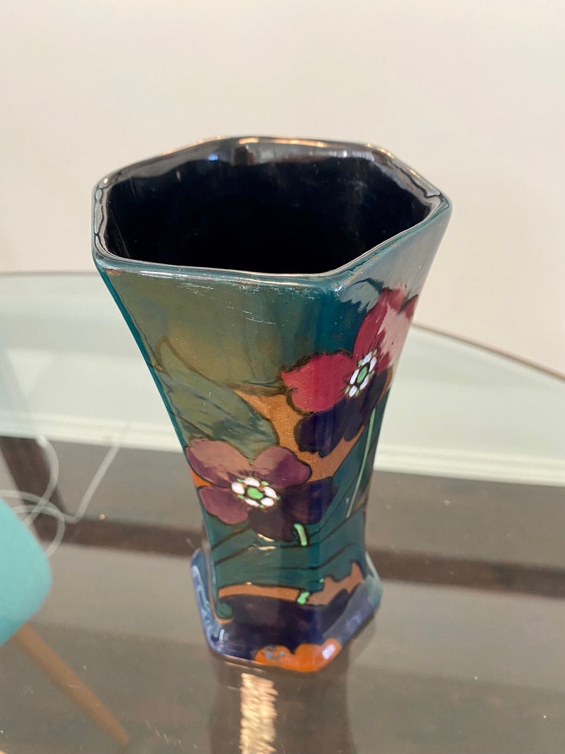 K&ouml;nnte beinhalten: Eine dunkelblaue und gr&uuml;ne Keramikvase mit geometrischer Form und floralem Design. Die Vase ist mit roten, violetten und wei&szlig;en Blumen verziert.
