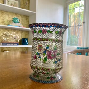 May include: A white cloisonné vase with a floral design in shades of pink, blue, green, and red. The vase has a delicate, intricate pattern and a clear, glass-like finish.