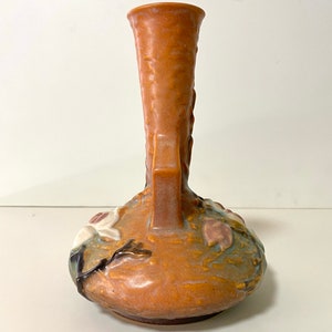 Może przedstawiać: Brązowy ceramiczny wazon z kwiatowym wzorem. Wazon ma szeroką podstawę i wąską szyjkę. Kwiaty są białe i r&oacute;żowe i są w reliefie.