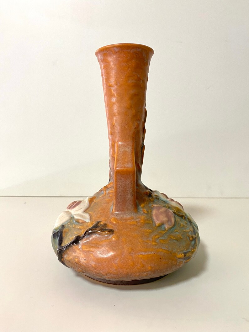 Może przedstawiać: Brązowy ceramiczny wazon z kwiatowym wzorem. Wazon ma szeroką podstawę i wąską szyjkę. Kwiaty są białe i r&oacute;żowe i są w reliefie.
