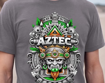 Puede incluir: Camiseta gris con un diseño azteca detallado. El gráfico incluye una máscara azteca estilizada, la palabra "AZTEC" y formas geométricas en verde, naranja y plata. El diseño está centrado en la camiseta.