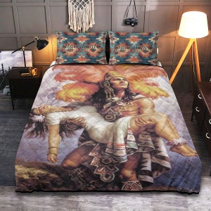 May include: A colorful quilt featuring a painting of a man carrying a woman. The man is wearing a feathered headdress and a colorful tunic. The woman is wearing a white dress. The quilt has a quilted pattern and is made of soft fabric.