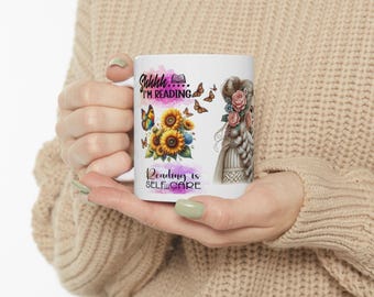 May include: White ceramic mug with a colorful design featuring a woman with flowers in her hair, butterflies, sunflowers, and the text "Shhh... I'm reading. Reading is self-care."