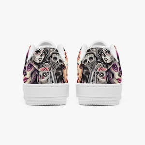 May include: White sneakers featuring a colorful Day of the Dead design. The artwork includes sugar skulls, roses, and portraits in shades of purple, pink, and black. The shoes have a classic low-top silhouette.