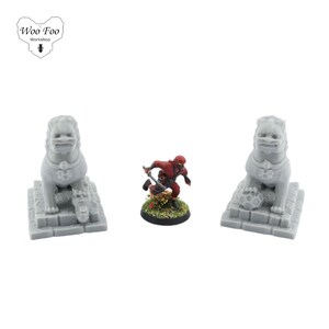 May include: Two grey stone lion statues with a red ninja figurine in the middle. The statues are on square bases and the ninja is on a round base with green grass.