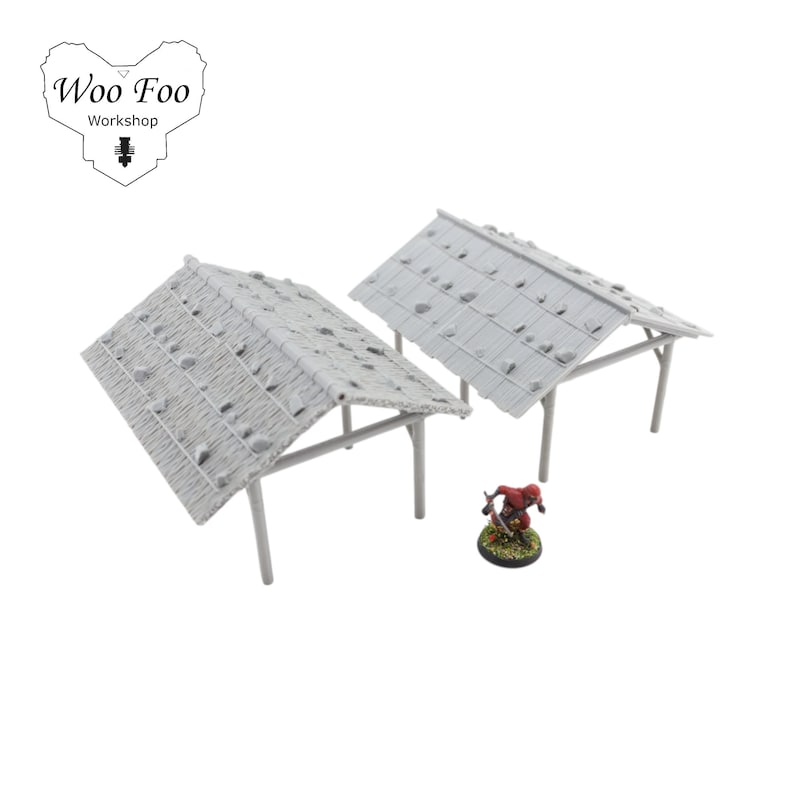 K&ouml;nnte beinhalten: Zwei Miniaturstrukturen in Grau mit Strohd&auml;chern und St&uuml;tzbeinen sowie eine kleine Figur einer Person in roter Kleidung. Die Strukturen sind f&uuml;r Tabletop-Spiele konzipiert. Das Logo "Woo Foo Workshop" befindet sich in der oberen linken Ecke.