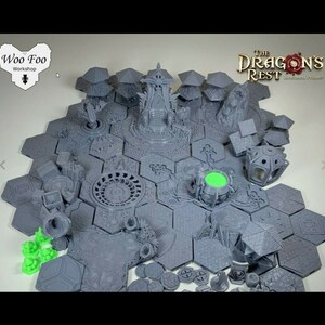 May include: A set of 3D printed gray and green tabletop game pieces, including hexagonal tiles, buildings, and figures. The tiles feature intricate designs and the figures are detailed. The set is labeled "The Dragon's Rest - Crafted Printers".