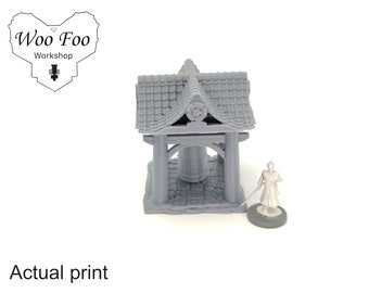May include: A gray 3D printed model of a Japanese temple bell tower with a tiled roof. The bell tower is about 4 inches tall and is sitting on a stone base. A miniature figure of a person is standing in front of the bell tower.