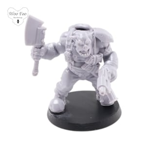 Puede incluir: Una miniatura de plástico gris de un guerrero Orco sosteniendo un hacha grande y una pistola. La miniatura está de pie sobre una base negra.