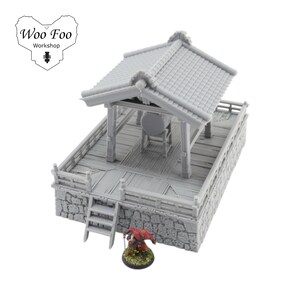 K&ouml;nnte beinhalten: Ein grauer Miniatur-Japan-Tempel mit Ziegeldach, Holzplattform und Steinsockel. Eine kleine Figur mit rotem Umhang steht in der N&auml;he. Das Woo Foo Workshop-Logo befindet sich oben links.