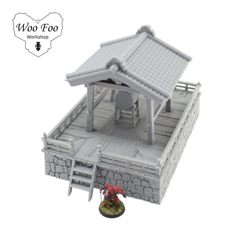 K&ouml;nnte beinhalten: Ein grauer Miniatur-Japan-Tempel mit Ziegeldach, Holzplattform und Steinsockel. Eine kleine Figur mit rotem Umhang steht in der N&auml;he. Das Woo Foo Workshop-Logo befindet sich oben links.