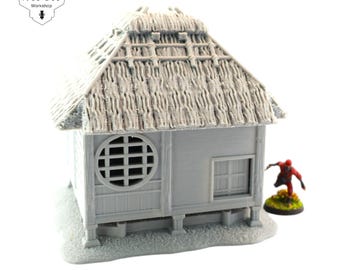 Op de afbeelding: Een gedetailleerd grijs model van een Japans huis met een rieten dak. Het huis heeft een klein raam en een deur. Het model staat op een grijze basis.