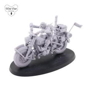 Puede incluir: Una miniatura de plástico gris de un goblin montando una motocicleta. La motocicleta tiene un sidecar y una bandera en la parte trasera. La miniatura está sobre una base negra.