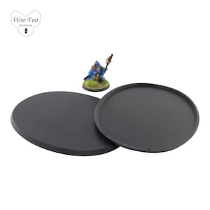 Op de afbeelding: Twee ronde zwarte plastic bases voor miniatuurfiguren. De bases zijn 25 mm in diameter en hebben een getextureerd oppervlak.