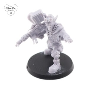 Puede incluir: Una figura en miniatura de plástico gris de una criatura parecida a un goblin que sostiene una gran arma. La figura está de pie sobre una base circular negra.