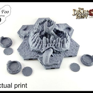 May include: A 3D printed gray tabletop game piece featuring a dragon's head with teeth and claws. The piece is surrounded by six hexagonal tiles with a geometric pattern. The piece is labeled "The Dragon's Rest Licensed Printer".