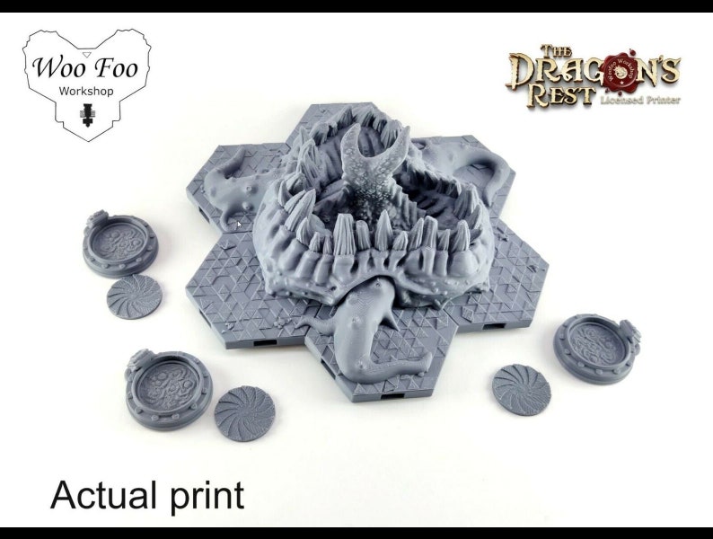 May include: A 3D printed gray tabletop game piece featuring a dragon's head with teeth and claws. The piece is surrounded by six hexagonal tiles with a geometric pattern. The piece is labeled "The Dragon's Rest Licensed Printer".