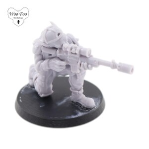 Puede incluir: Una figura en miniatura de plástico gris de un soldado arrodillado sosteniendo un rifle. El soldado lleva un casco y tiene una mira telescópica en el rifle.