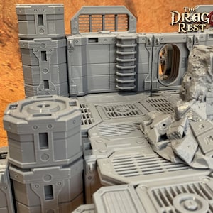 Può includere: Un modello stampato in 3D di una città futuristica con muri grigi, una scala, una finestra e un cumulo di macerie. Il modello è progettato per giochi da tavolo ed è etichettato "The Dragon's Rest - Designed & Printed".