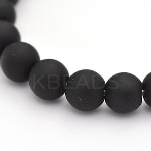 May include: Close-up of a strand of matte black beads. The beads are round and have a slightly textured surface. The text "KBeads" is visible on the beads. The beads are strung together, suggesting a bracelet or necklace.