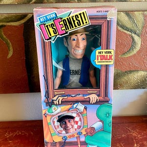 May include: A Kenner Hey Vern, It's Ernest! action figure in its original packaging. The box features a window displaying the Ernest doll wearing a tan hat, grey t-shirt, and blue vest. The box art includes the text Hey Vern, It's Ernest! and Hey Vern, I Talk Knowhutimean? with a graphic of a television set.