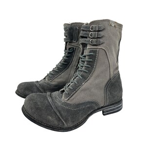 May include: A pair of gray combat boots with a distressed look. The boots feature a combination of suede and canvas materials, with lace-up closures and buckle details. The soles are dark gray, and the boots have a worn appearance.