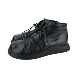 May include: A pair of black leather ankle boots featuring a smooth, rounded toe, a thick black rubber sole, and a black drawstring lace system with a plastic toggle closure. The leather upper has a soft, slightly creased texture throughout.