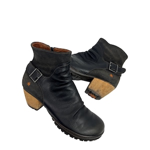 May include: Black leather ankle boots with a side zipper and buckle detail. The boots have a wooden heel and a dark gray suede collar. An orange star is stitched on the side of the heel. The boots are shown on a white background.