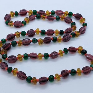 May include: A long necklace made of purple, green, and orange glass beads. The beads are strung on a thin cord and are arranged in a repeating pattern.