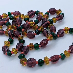 May include: A long necklace made of purple, amber, and green glass beads. The beads are strung on a thin orange cord.