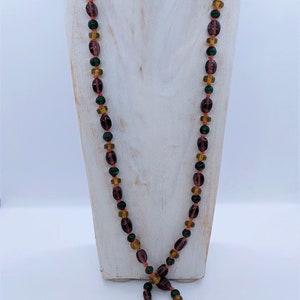 May include: A long necklace made of purple, green, and orange glass beads. The beads are oval shaped and have a glossy finish.