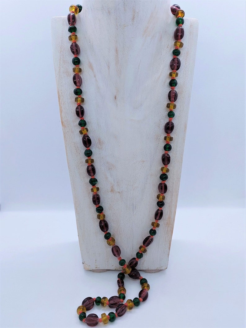 May include: A long necklace made of purple, green, and orange glass beads. The beads are oval shaped and have a glossy finish.