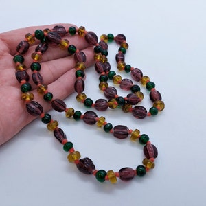 May include: A long necklace made of purple, green, and orange glass beads. The beads are oval shaped and have a glossy finish.