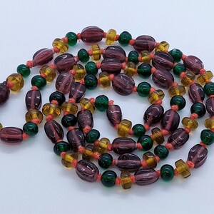 May include: A long strand of beads with a mix of purple, green, and amber glass beads. The beads are strung on a thin cord.