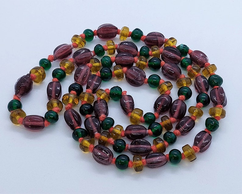 May include: A long strand of beads with a mix of purple, green, and amber glass beads. The beads are strung on a thin cord.