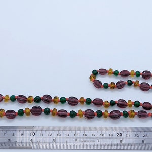 May include: A long necklace made of glass beads in shades of purple, orange, and green. The beads are strung on a clear cord and are approximately 30 inches long.