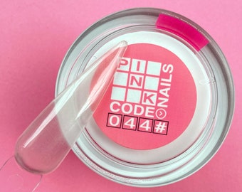 Puede incluir: Un tarro rosa con tapa blanca que contiene un polvo acrílico transparente. El tarro tiene una etiqueta rosa con el texto "PINK CODE NAILS 044#" en él.