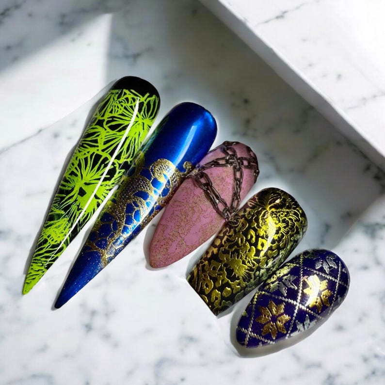 May include: Five different nail designs featuring gold foil accents. The designs include a green and gold floral pattern, a blue and gold snake pattern, a pink and gold chain pattern, a brown and gold leopard print pattern, and a blue and gold geometric pattern.